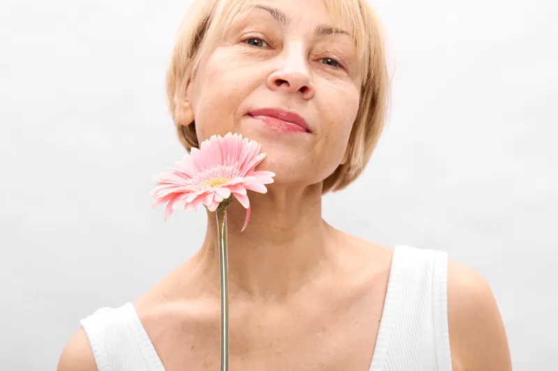 Woman portrait closeup, smiling, holding a pink gerbera flower on a vase, spring beauty and freshness, soft studio light on white background