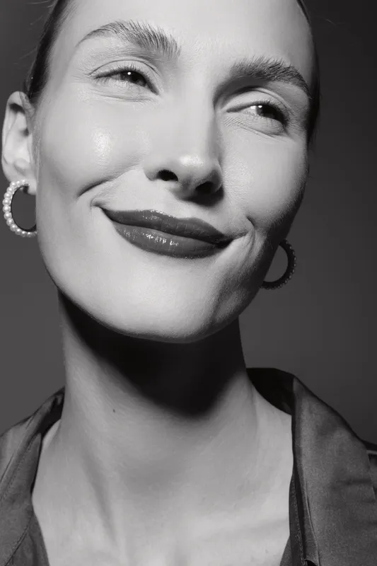 Close-up of a smiling Caucasian woman with pale skin wearing hoop earrings and dark lipstick in black and white. Concept of beauty and elegance.