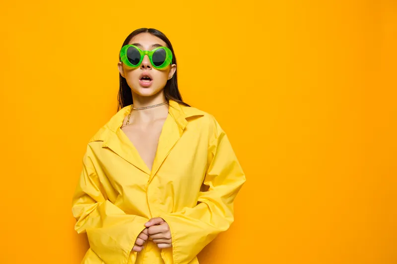Изолированная гламурная женщина в студии с солнцезащитными очками и выразительным жестом излучает радость и стиль