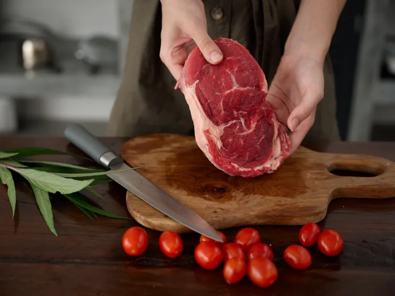 Женщина с ножом в руке режет свежее мясо для жарки на кухне