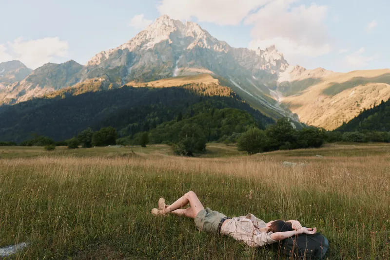 Woman rests in a sunlit meadow with distant mountains, relaxed pose and carefree lifestyle, natural colors, outdoor escape