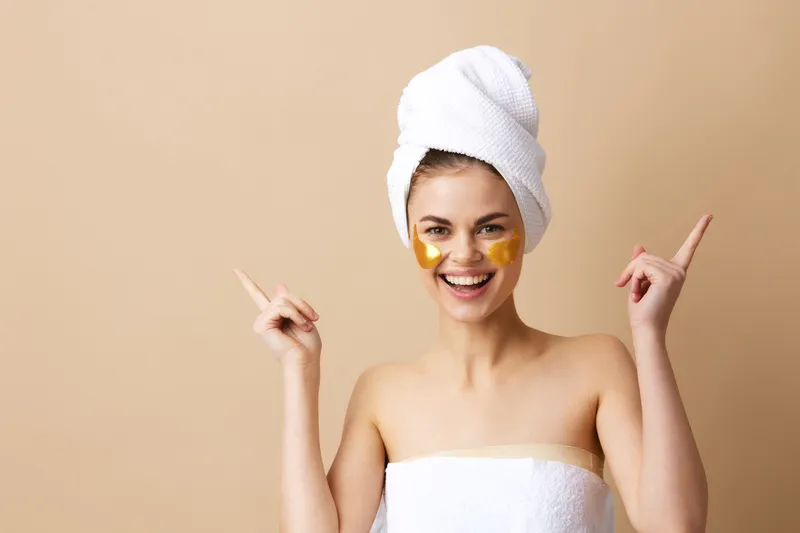 Молодая женщина с патчами для ухода за кожей, веселящаяся после душа на изолированном фоне
