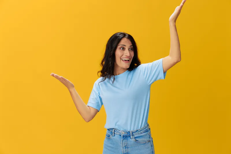 Женщина показывает сигнал, улыбается с зубами, эмоциональный портрет в синей футболке на желтом фоне