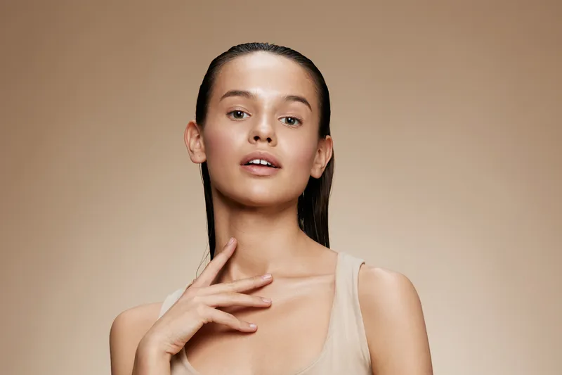 Ethereal beauty portrait of a young model with wet hair, showcasing fresh skin and a subtle pose against a neutral background, embodying elegance and simplicity