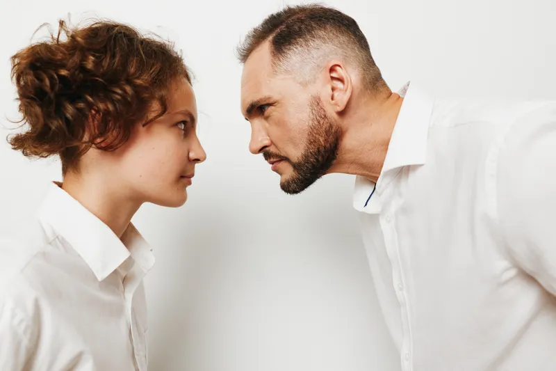 A focused professional man and a colleague face each other on a solid colored background, expressing tension and concentration, signaling business dialogue and emotions in a corporate setting.
