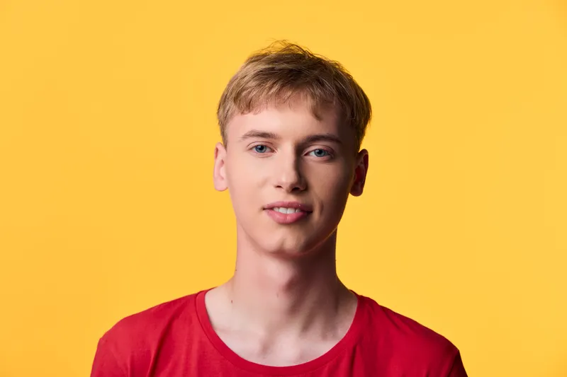 Young man wearing a red shirt against a bright yellow background, studio shot with clear lighting, casual expression, clean composition suitable for fashion, lifestyle, or model showcase.