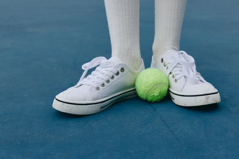 A young athlete standing on a blue tennis court with a green tennis ball, wearing white sneakers and socks, showcasing a passion for sports and healthy lifestyle