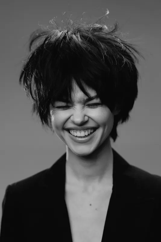 Smiling woman with tousled hair in black and white portrait expressing joy and happiness in minimalist style