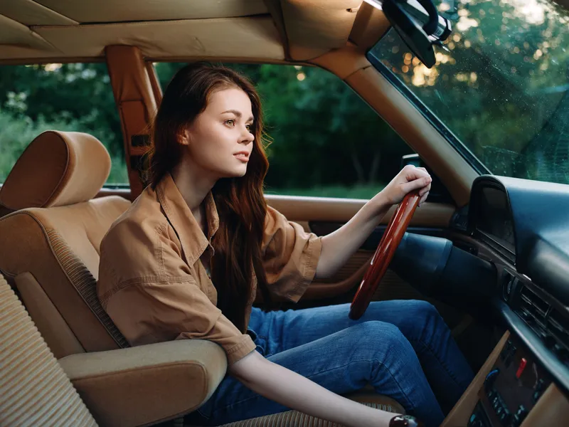 Young woman driving an old-fashioned car, showcasing a relaxed mood in a natural setting, with a focus on emotions and vintage style.