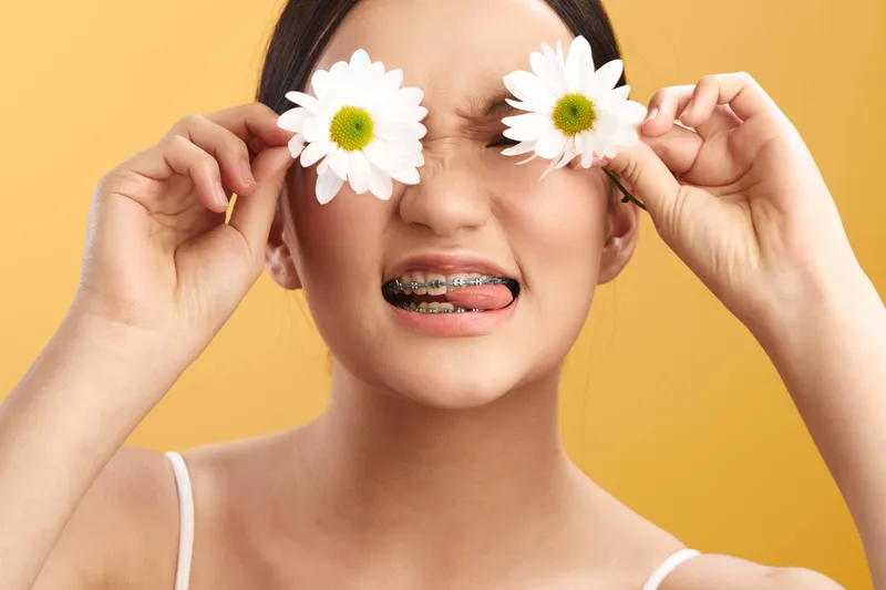 cheerful asian woman is playfully holding flowers over her eyes in a bright studio, creating a whimsical moment with a warm smile and a lighthearted, fresh vibe.