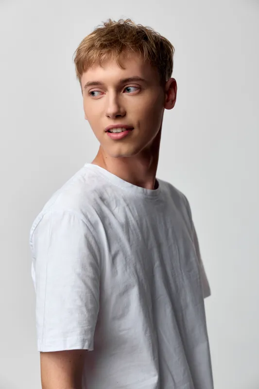 Casual man in a white t-shirt poses in a studio with a thoughtful gaze, clean neutral backdrop, soft lighting, and a natural, relaxed mood.