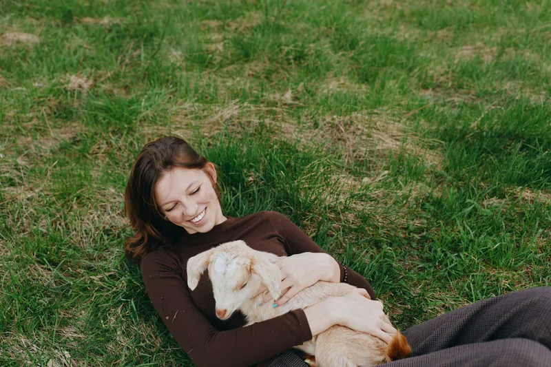 Bright woman outdoors, lying on grass with a friendly dog, warm sunlight, relaxed posture, casual outfit, natural tones, fresh air, tranquil park ambiance, and playful energy, candid smiles, tender