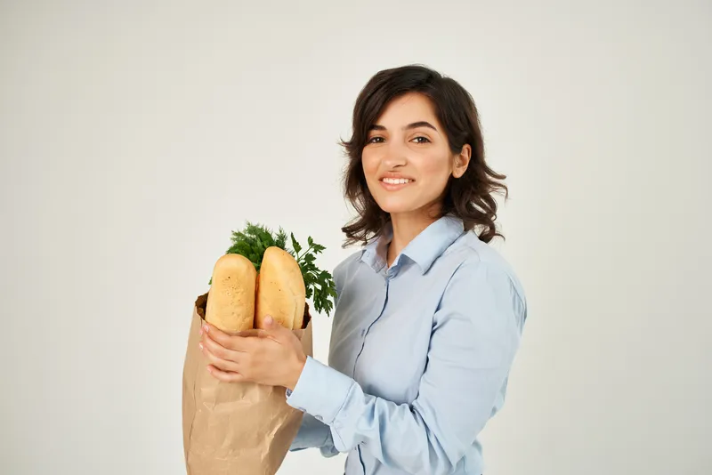 Веселая женщина с пакетом продуктов в супермаркете: здоровая еда, овощи