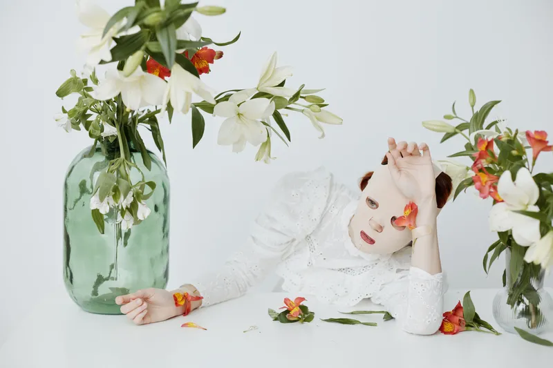 Female model in floral arrangement, wearing white dress, conveying feelings of tranquility and beauty in vibrant floral setting with soft colors