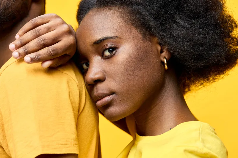 Portrait of a young Black woman with natural hair in yellow attire, conveying emotion against a vibrant yellow background, showcasing connection and warmth