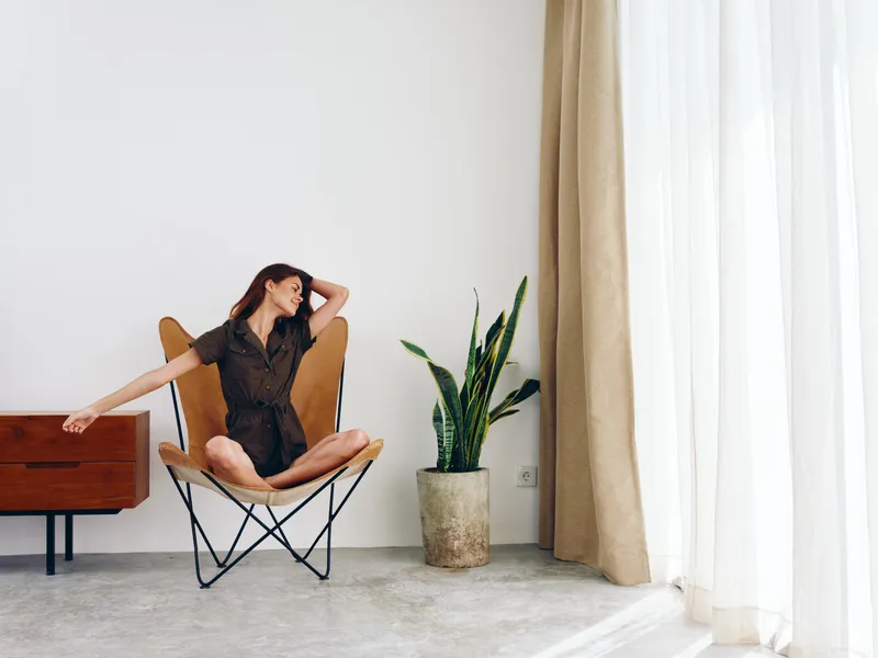 Женщина сидит в кожаном кресле у окна и улыбается