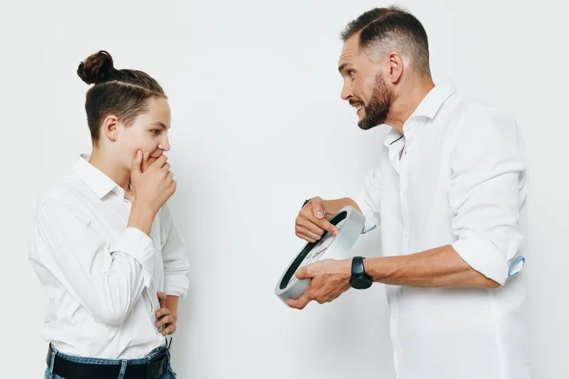 A professional man and a younger colleague share a thoughtful moment against a clean colored backdrop, conveying business focus, emotion, and teamwork in a modern corporate setting.