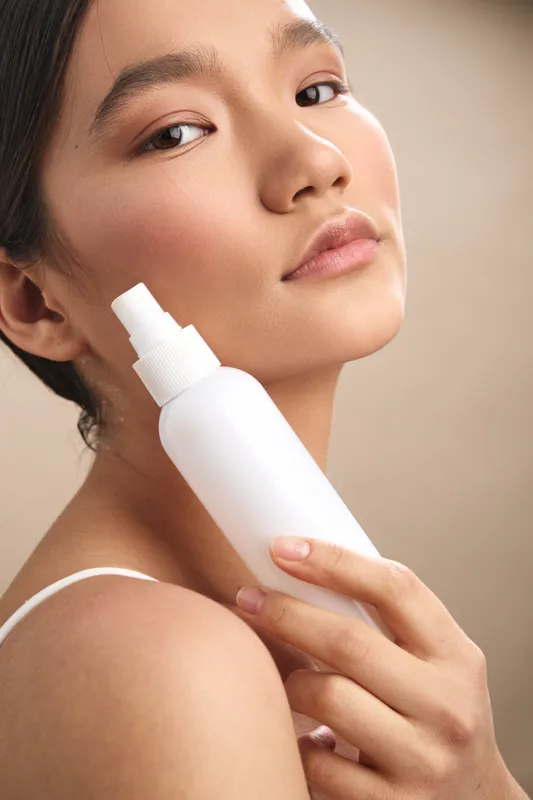 asian woman holds a spray bottle near her face, showcasing a skincare moment in soft studio light, suggesting calm selfcare and a fresh beauty routine.