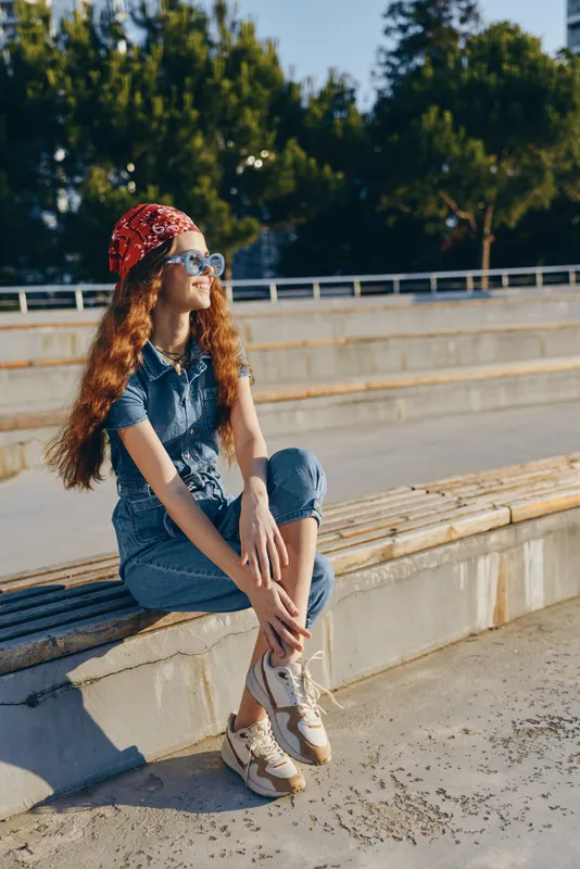 lifestyle woman wearing modern boho-western denim street style outfit with sunglasses and red bandana, sitting outdoors with film color warmth and casual vibe