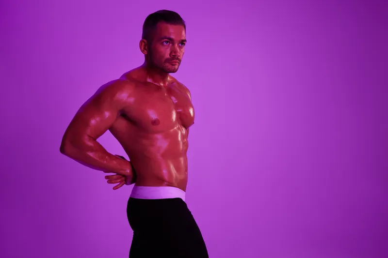 Спортивный мужчина, бодибилдер в трусах, с обнаженным торсом и прессом, в полный рост на фоне, фитнес-занятия, фиолетовый цветной свет