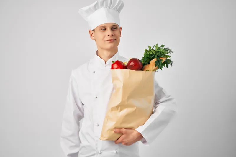 Мужчина с пакетом продуктов для здорового питания работает на кухне ресторана