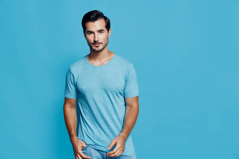 Handsome man in casual blue t-shirt poses confidently against a vibrant blue background, showcasing a stylish look and a relaxed demeanor in this studio portrait.