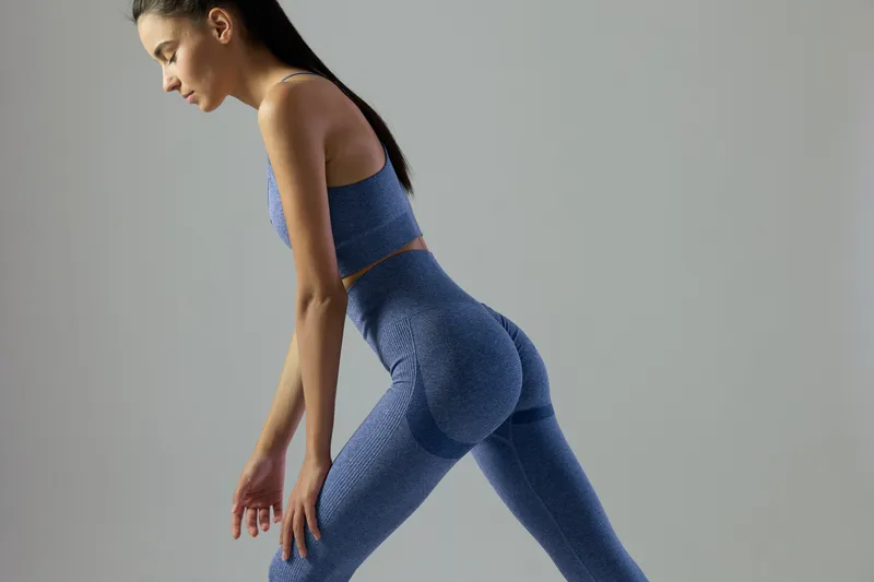 Woman sport fitness stretching in blue activewear, slim body, focused pose, indoor studio with neutral background, athletic lifestyle concept.