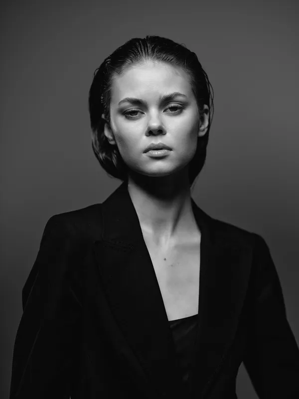 Black and white portrait of serious woman wearing dark jacket with neutral expression and minimalistic background