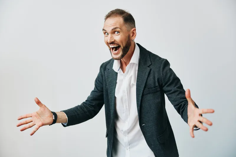 Professional man in business attire on a solid colored background, expressing joyful excitement with open arms, conveying confidence and energy in a dynamic pose.