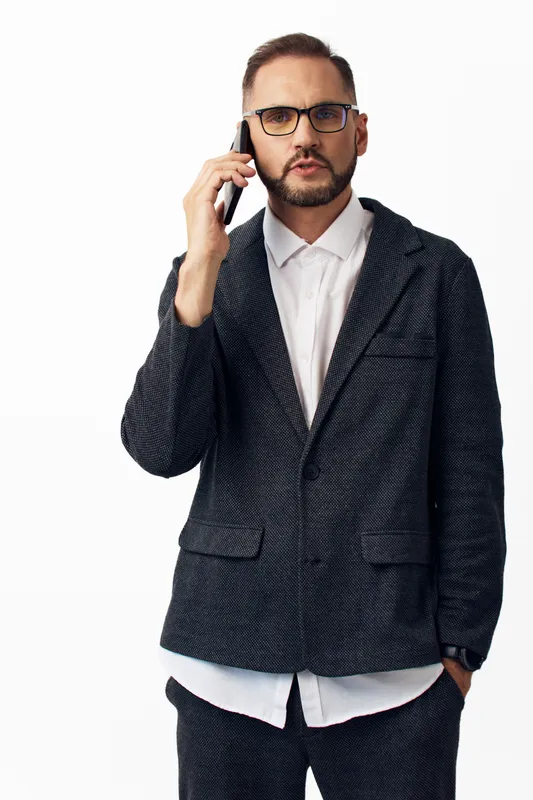A confident business professional stands on an isolated white background, speaking on a mobile phone, projecting focus, determination, and calm authority with a poised, executive presence.
