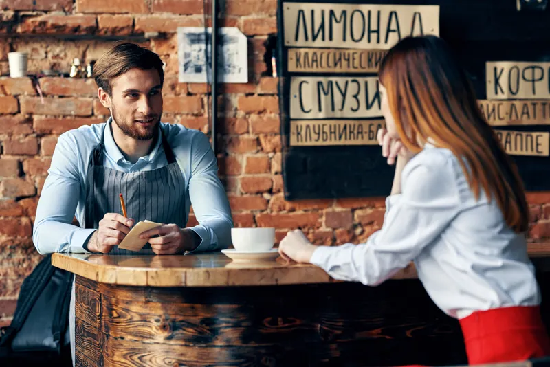 Официант-шеф принимает заказ у молодой женщины в рубашке на чашку кофе в кафе-ресторане