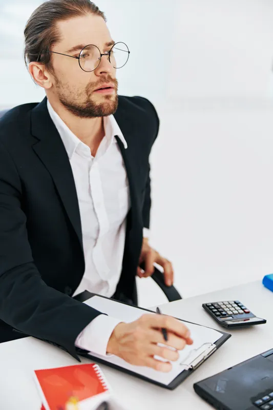Мужчина в костюме с документами работает в офисе за ноутбуком, используя технологии