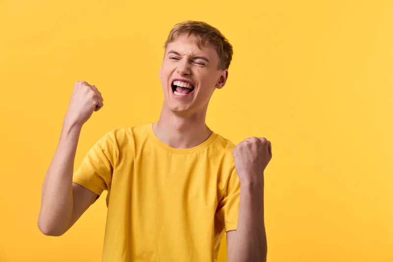 Excited man, arms raised in celebration against a bright yellow background, conveys triumph, energy, and happiness through bold emotion and dynamic gesture suitable for lifestyle and advertising