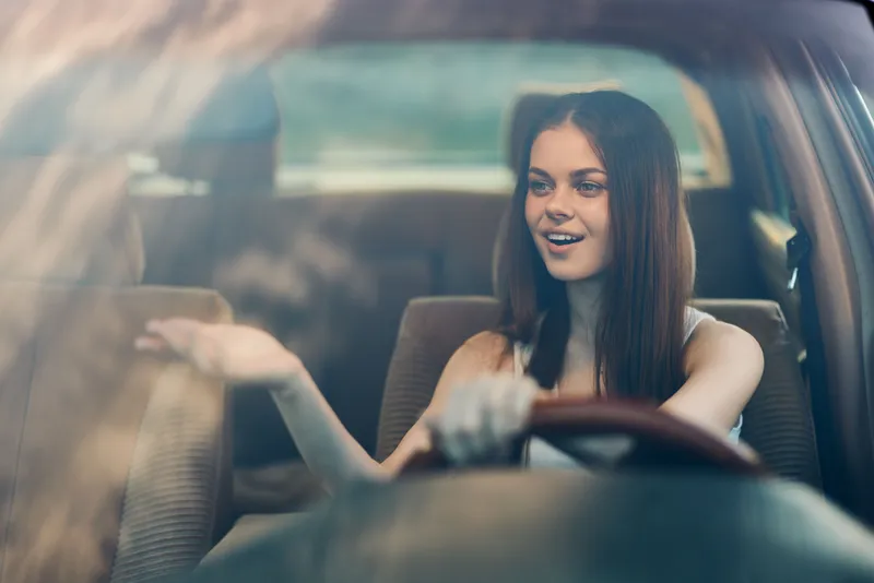 Happy young woman driving a car, enjoying the ride with a cheerful expression and stylish attire, green background, capturing the concept of freedom and adventure.