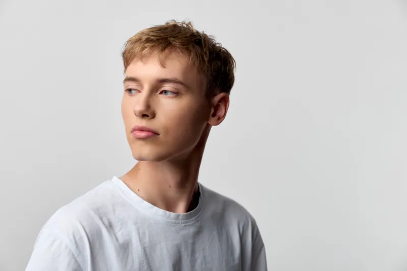 Young man wearing a tshirt, looking to the side with a thoughtful expression, studio lighting, clean background, casual stylish mood suitable for fashion, lifestyle or product shoots