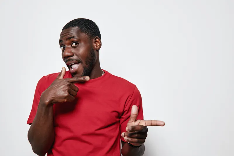 African American man with dark skin wearing red t shirt pointing fingers and smiling on white background for casual gesture and positive expression concept.
