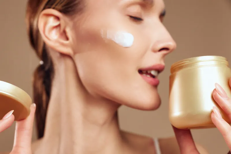 A woman applies moisturizer cream on her face, showcasing a focused skincare routine. Soft, warm lighting highlights self care, calm beauty rituals, and healthy skin.