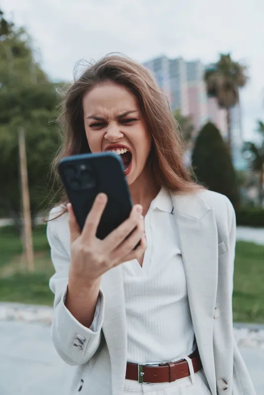 Businesswoman expressing frustration while using a smartphone outdoors, showcasing elegance and determination in a modern urban setting.