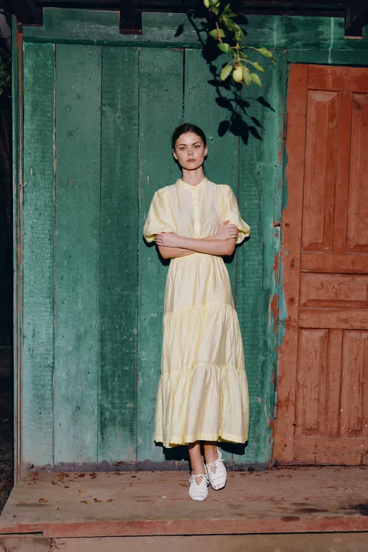 woman in yellow dress standing against rustic wooden green wall portrait with arms crossed authentic inclusive natural light