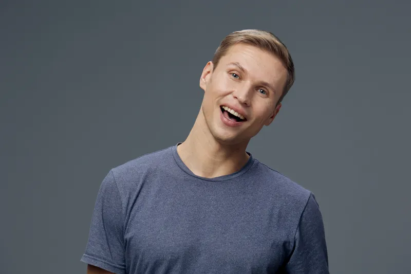 smiling man with gray t-shirt tilt head upbeat happy facial expression isolated on solid gray background studio portrait digital detox concept
