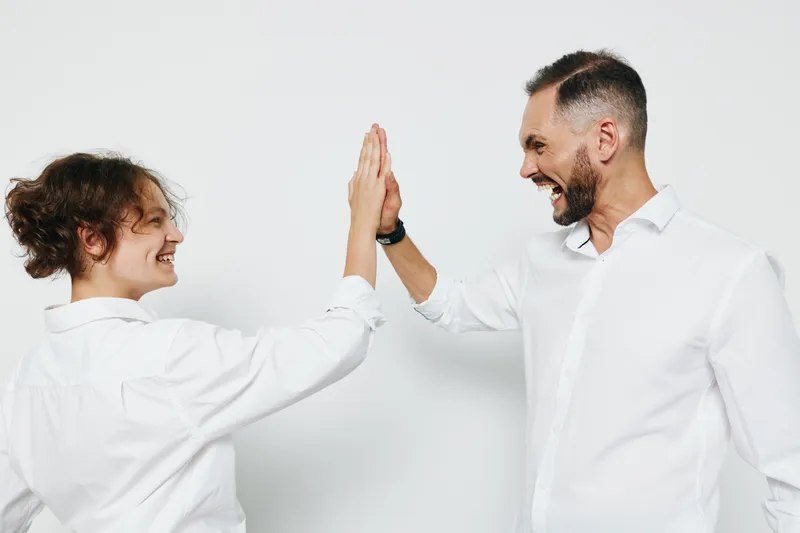 A professional man and colleague share a celebratory high five on an isolated colored background, conveying confidence, energy, and teamwork in a modern business scene.