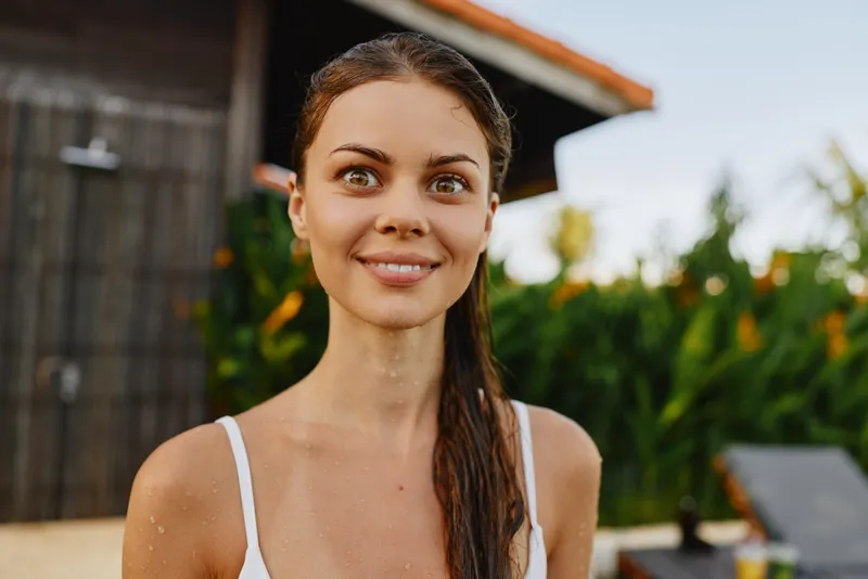 Cheerful woman outdoors, smiling with sunlit face, casual summer style, bright natural colors, lush garden background, relaxed vibe, warm breeze, candid portrait