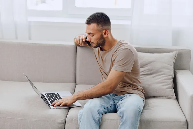 Focused man working on a laptop at home, showcasing modern remote work trends with a comfortable and casual vibe in a bright, minimalistic setting.