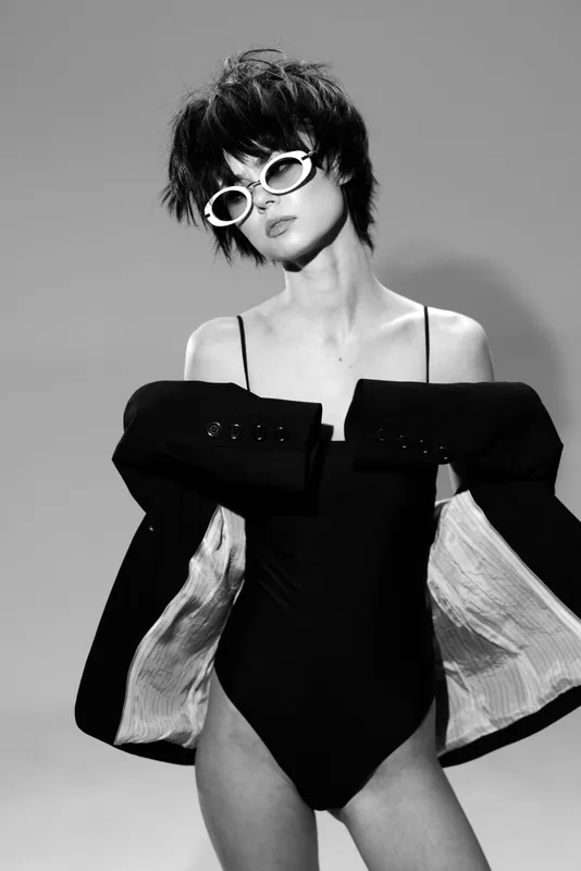 Black and white portrait of a stylish woman wearing sunglasses and a jacket, showcasing fashion and attitude.