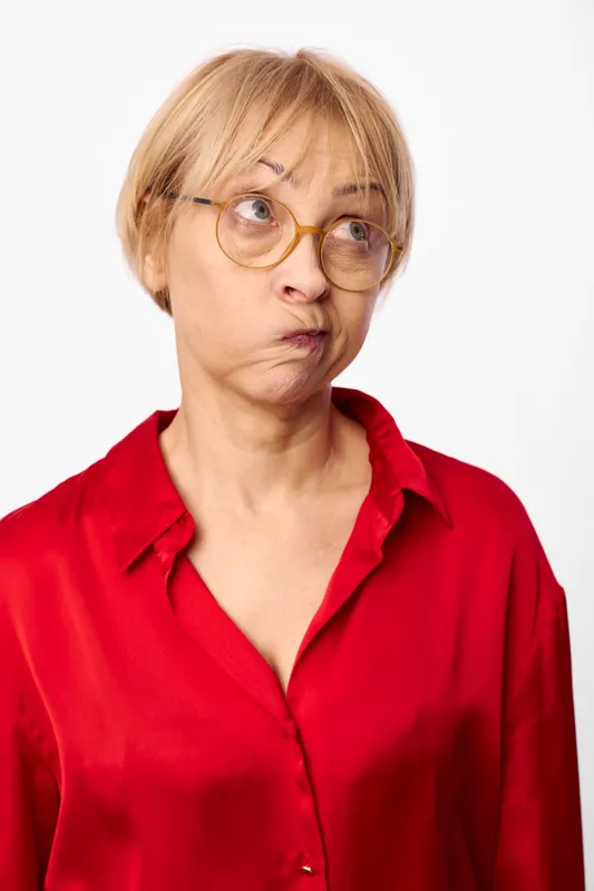 Elderly woman, wearing glasses, looks surprised and shocked, making an intense expression in a portrait, red shirt, studio closeup against white background