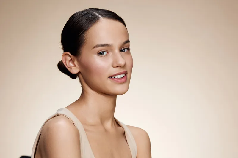 Young woman with a natural smile, featuring a minimalist style on a soft beige background, conveying beauty and confidence
