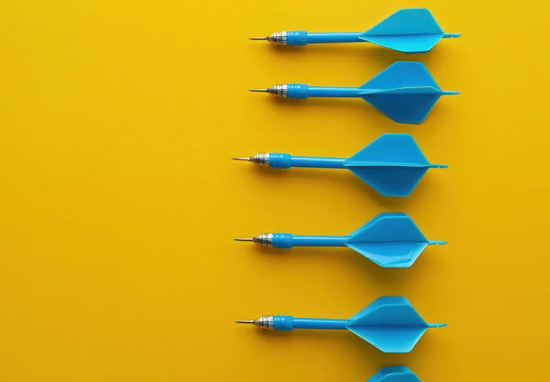 Ряд синих стрелок-дротиков, выстроенных в линию на ярко-желтой поверхности, символизирующих точность и достижение цели