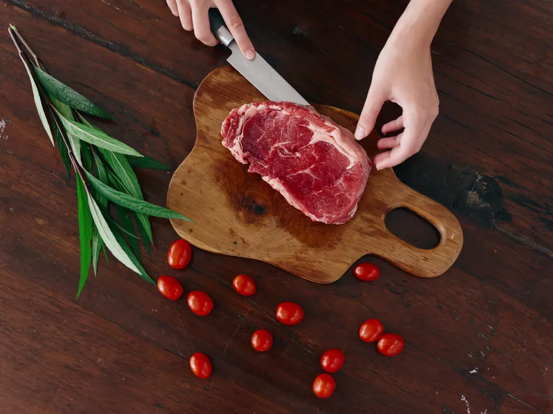 Женщина с ножом в руке нарезает свежее мясо для стейка, которое будет запекаться на кухне