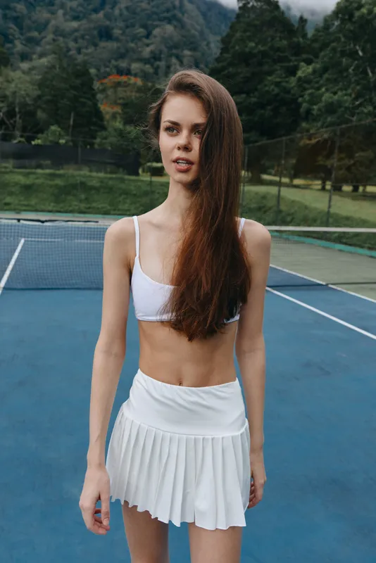 Young woman in white sportswear on a tennis court, exuding confidence and energy, showcasing athleticism and healthy lifestyle with vibrant green background