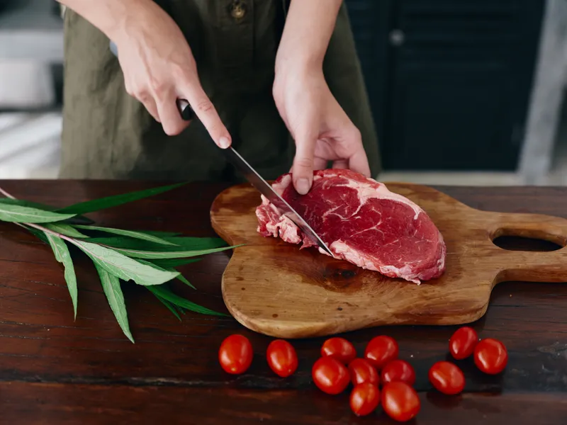 Женщина с ножом в руке нарезает свежее мясо стейка для жарки на кухне